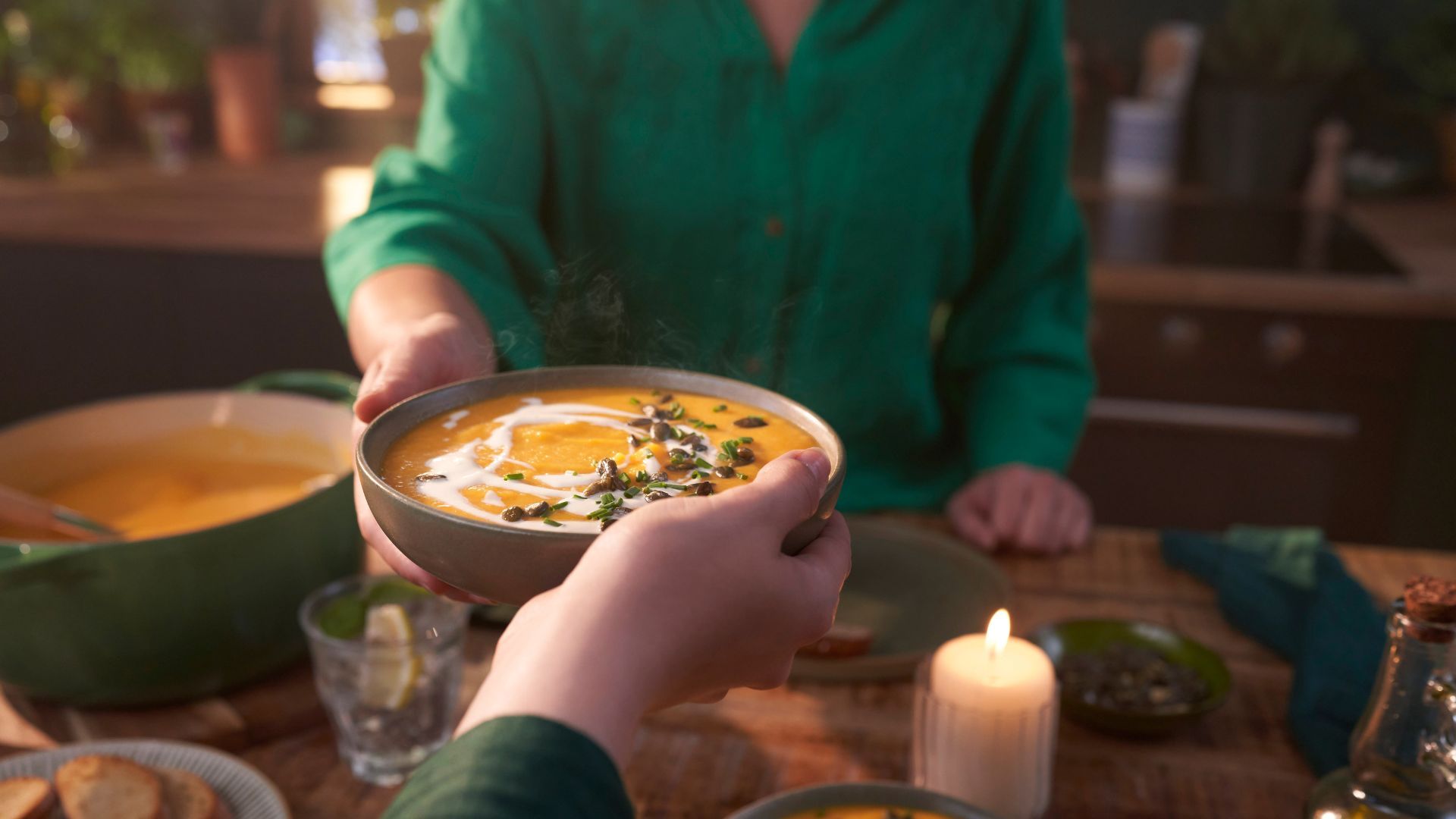 Cropped hand handing a bowl of pumpkin soup over a wooden table