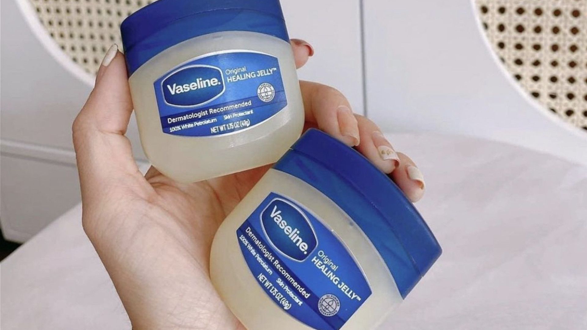 Close up of a woman's hand. She is holding two jars of Vaseline Original Healing Jelly.