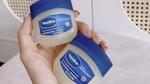 Close up of a woman's hand. She is holding two jars of Vaseline Original Healing Jelly.