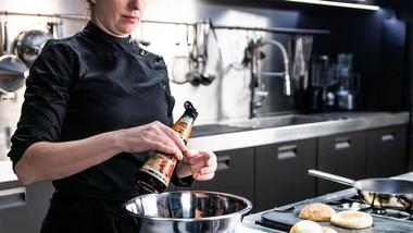 Female chef in professional kitchen pouring bottle of Knorr Intense Flavours into mixing bowl.