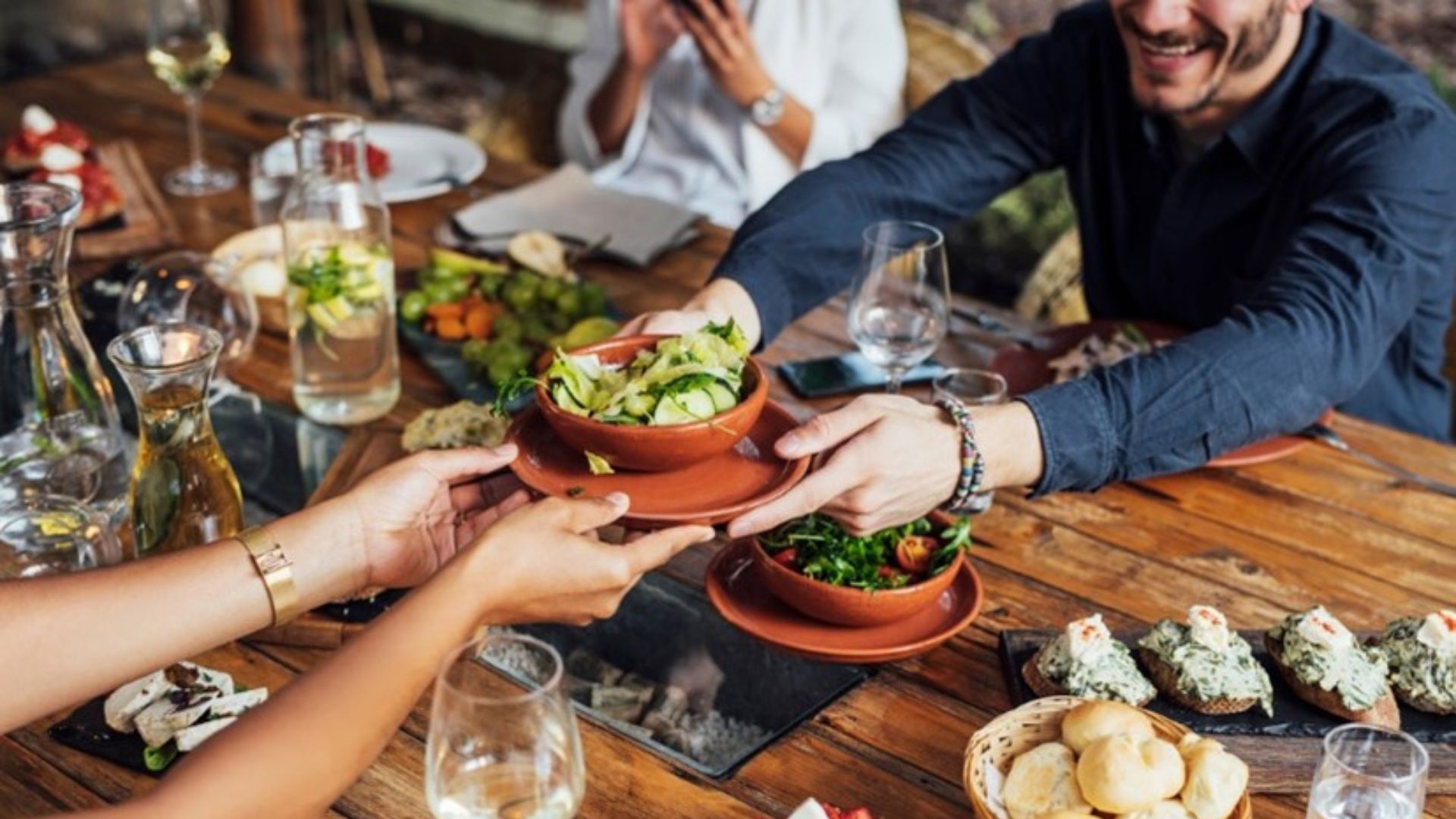 Hands of cropped unrecognisable woman and man passing salad bowl on the dining table 
