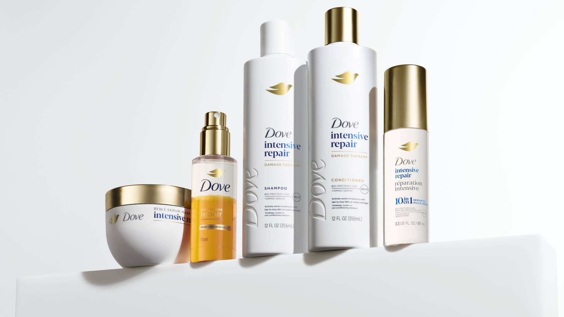 Five products from Dove’s Damage Therapy range for damaged hair repair. White bottles with premium gold accents.