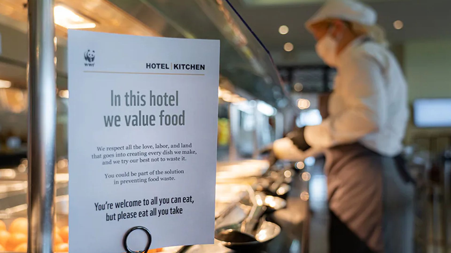 A chef working in a kitchen with a clear sign declaring that the kitchen works to ensure food is not wasted