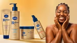 A campaign image for Vaseline Radiant X, featuring a Black woman laughing, and a range of four products in gold and blue packaging including body lotions and body oil.