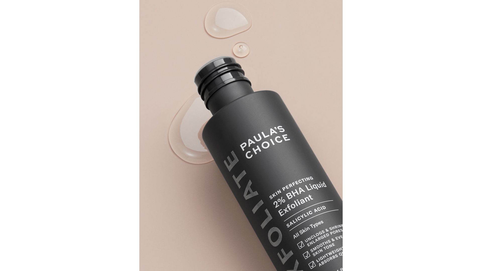 A bottle of Paula’s Choice Liquid Exfoliant lying on its side with drops of the product visible.