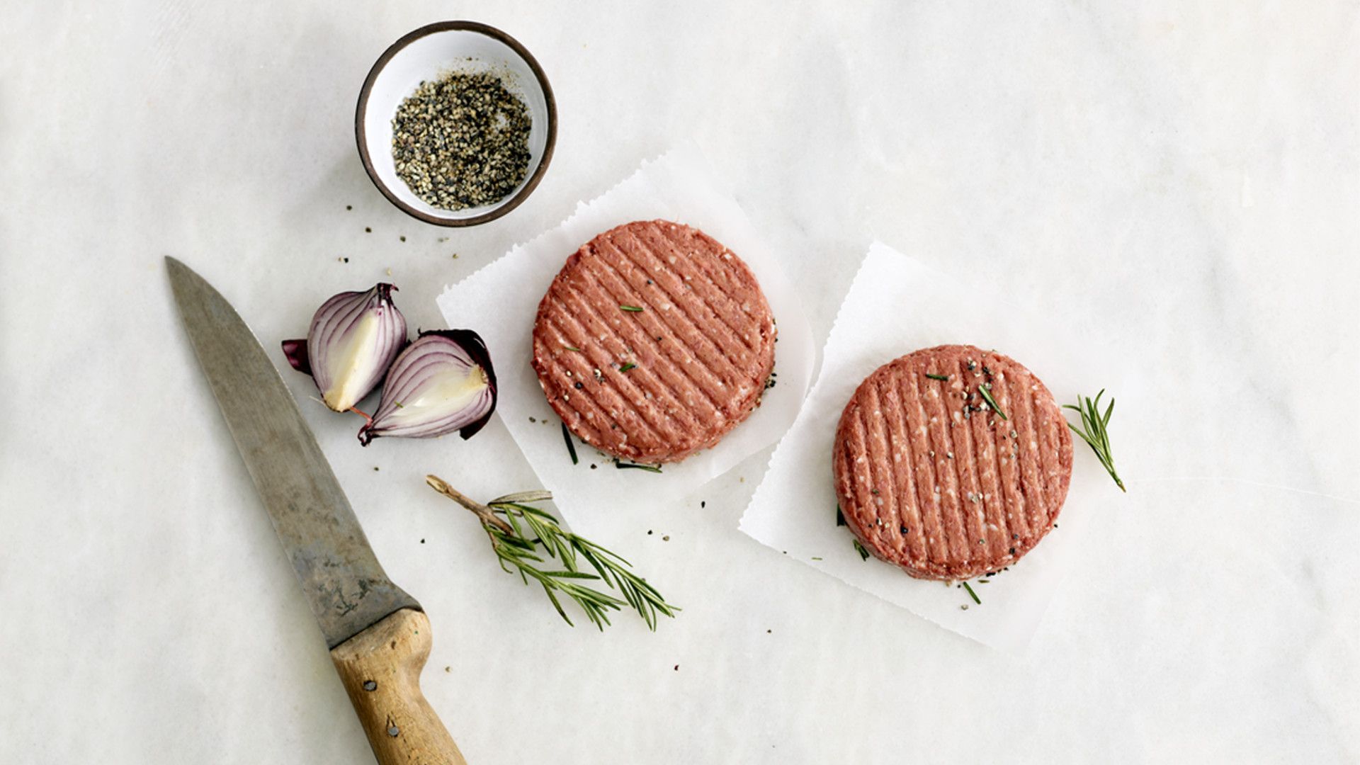 Two of The Vegetarian Butcher’s raw burgers on a plate with pepper and garnish being prepped for cooking