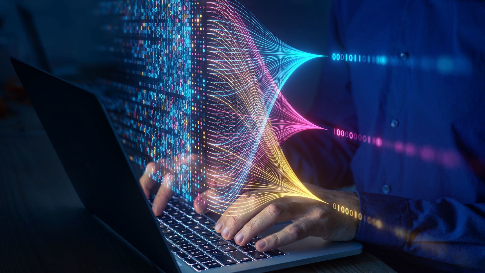 A silver laptop with black keys, hands on a keyboard, overlaid with an array of colourful digital code to indicate technology.