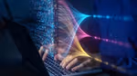 A silver laptop with black keys, hands on a keyboard, overlaid with an array of colourful digital code to indicate technology.