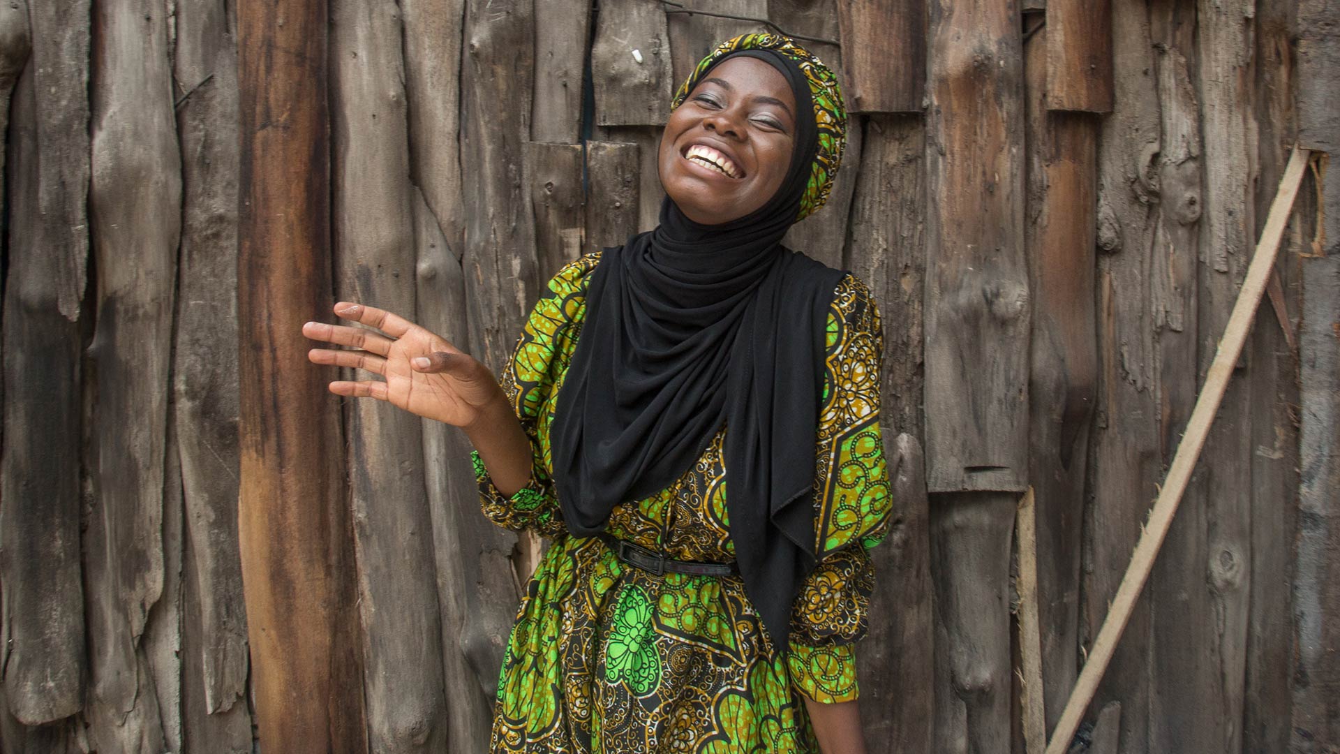 A woman standing beside a wooden fence and smiling