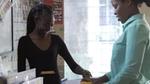 Two women interacting in a store setting. One is wearing a black top and smiling, and the other woman is dressed in a light teal shirt.