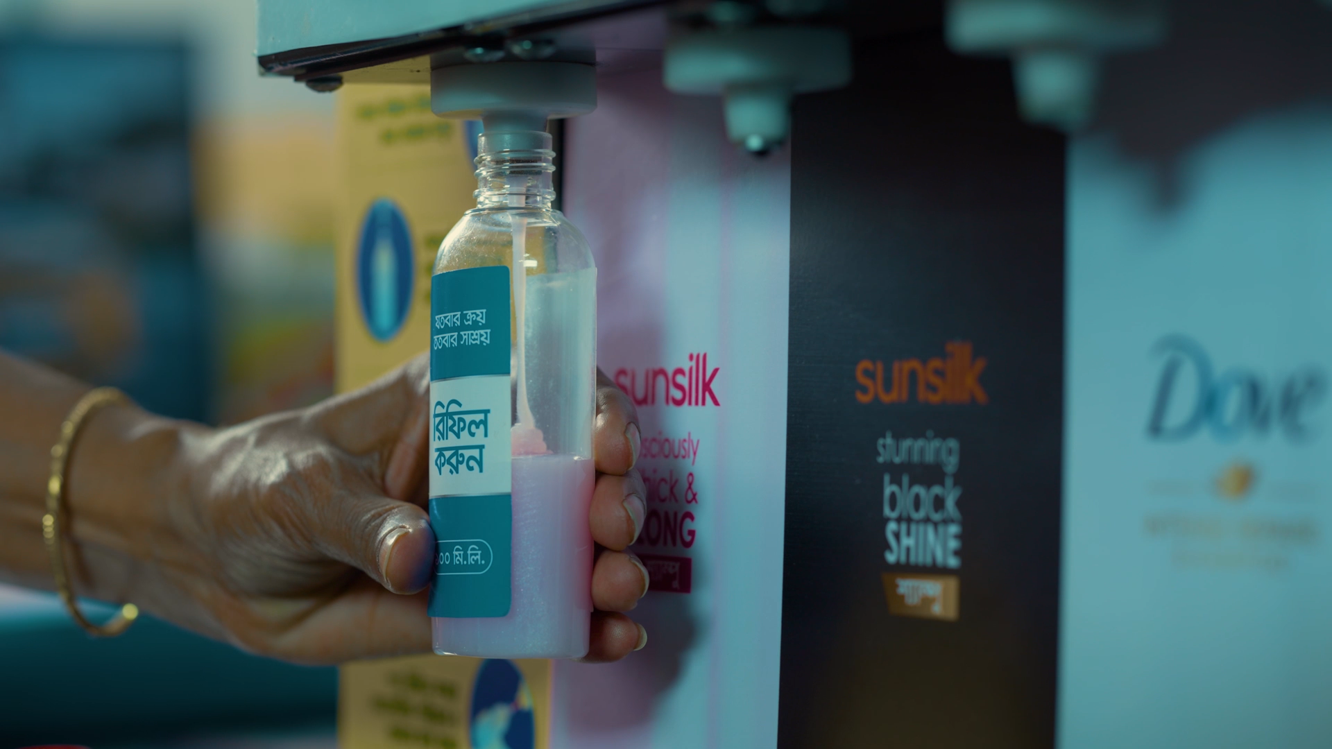 A refill station with Unilever brands including Sunsilk and Dove. The image shows a bottle being filled with pink Sunsilk product and a person holding the bottle.