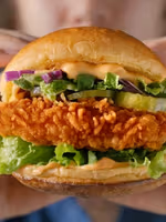 Person holding a crispy chicken sandwich with lettuce and pickles.