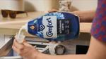 Person pouring Comfort fabric conditioner into bottle cap ready to put in washing machine.