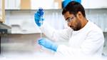 A person in a science lab wearing gloves and eye protection adding liquid to a test tube.
