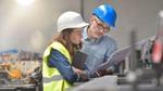 Two employees dressed in hard hats having a conversation in a factory