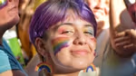 Someone smiling among a group of people with a rainbow-painted face and rainbow earrings.
