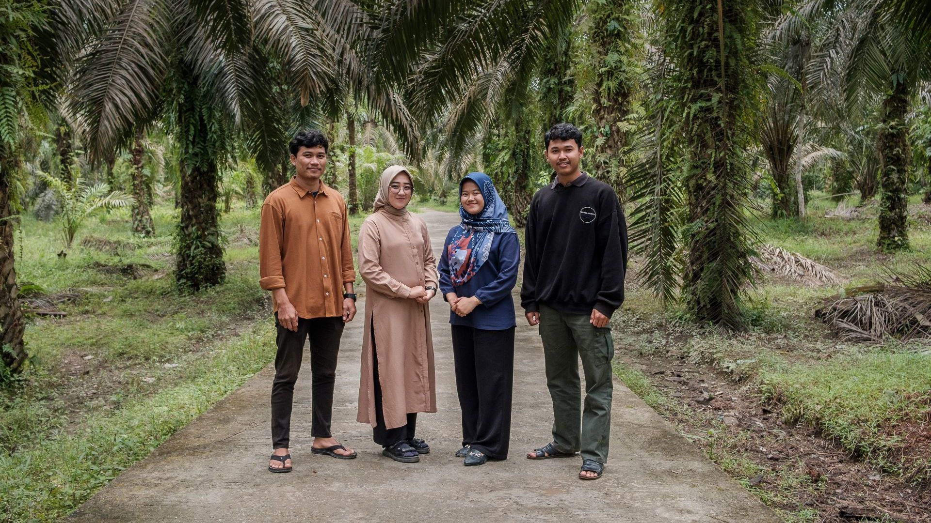 A photograph of four people – two men and two women – stand on a path beneath palm trees.
