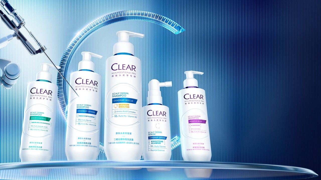 Five white bottles from the Clear scalp care range displayed on a futuristic, blue lit surface. The bottles vary in height and shape, each with coloured labels indicating different shampoo and treatment formulas. A laboratory style robotic arm and curved light elements in the background create a high tech, clinical atmosphere.
