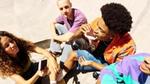 Four casually dressed individuals sitting on a concrete surface, possibly at a skate park, eating ice creams.