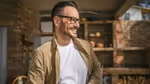 Smiling man with glasses outdoors in sunlight.