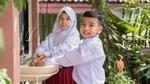 Two smiling Indonesian schoolchildren wash their hands at an outdoor sink.