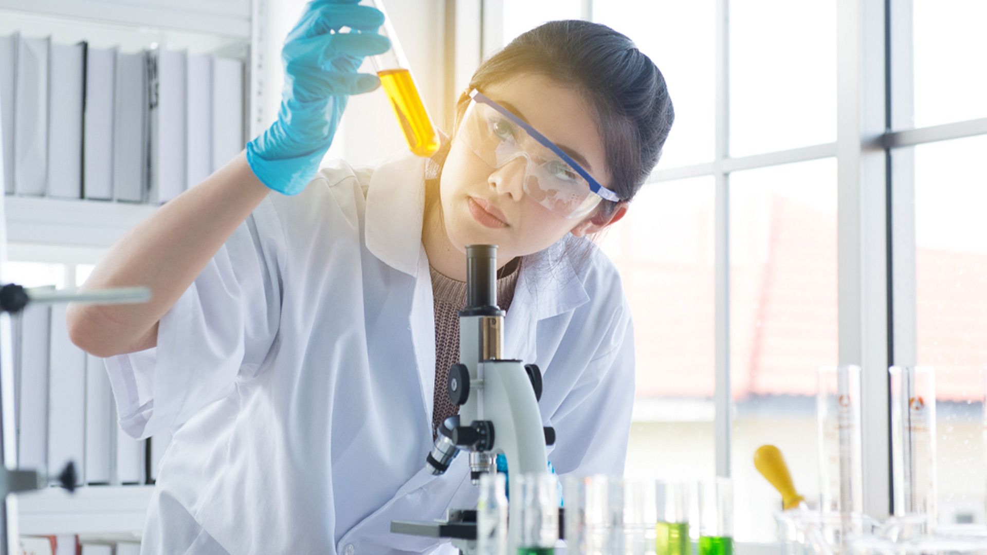 lady in science lab wearing lab coat looking at a yellow test tube