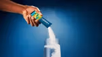 A hand pouring Liquid I.V. Hydration Multiplier powder from a sachet into a glass of water, with the powder visibly mixing against a blue background.