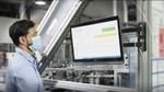 Man in front of two computer screens with a factory setting blurred in the background