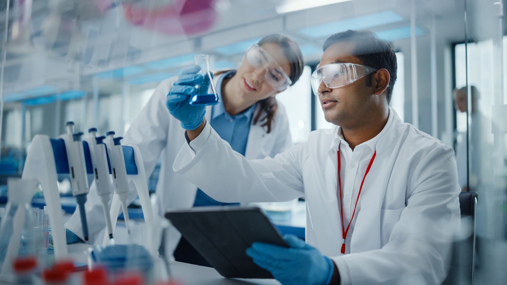 Male scientist and female scientist consider a flask of blue chemicals in a lab testing environment.