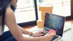 Young woman sitting in front of a laptop and using a credit card to pay for shopping online.