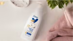 Dove Body Love Cream Oil lotion bottle beside pink towels and green leaves.