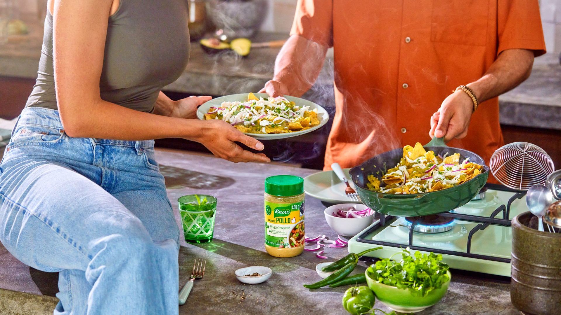 A man and a woman cooking and plating up a dish, with a Knorr Chicken Bouillon Powder jar on the counter.