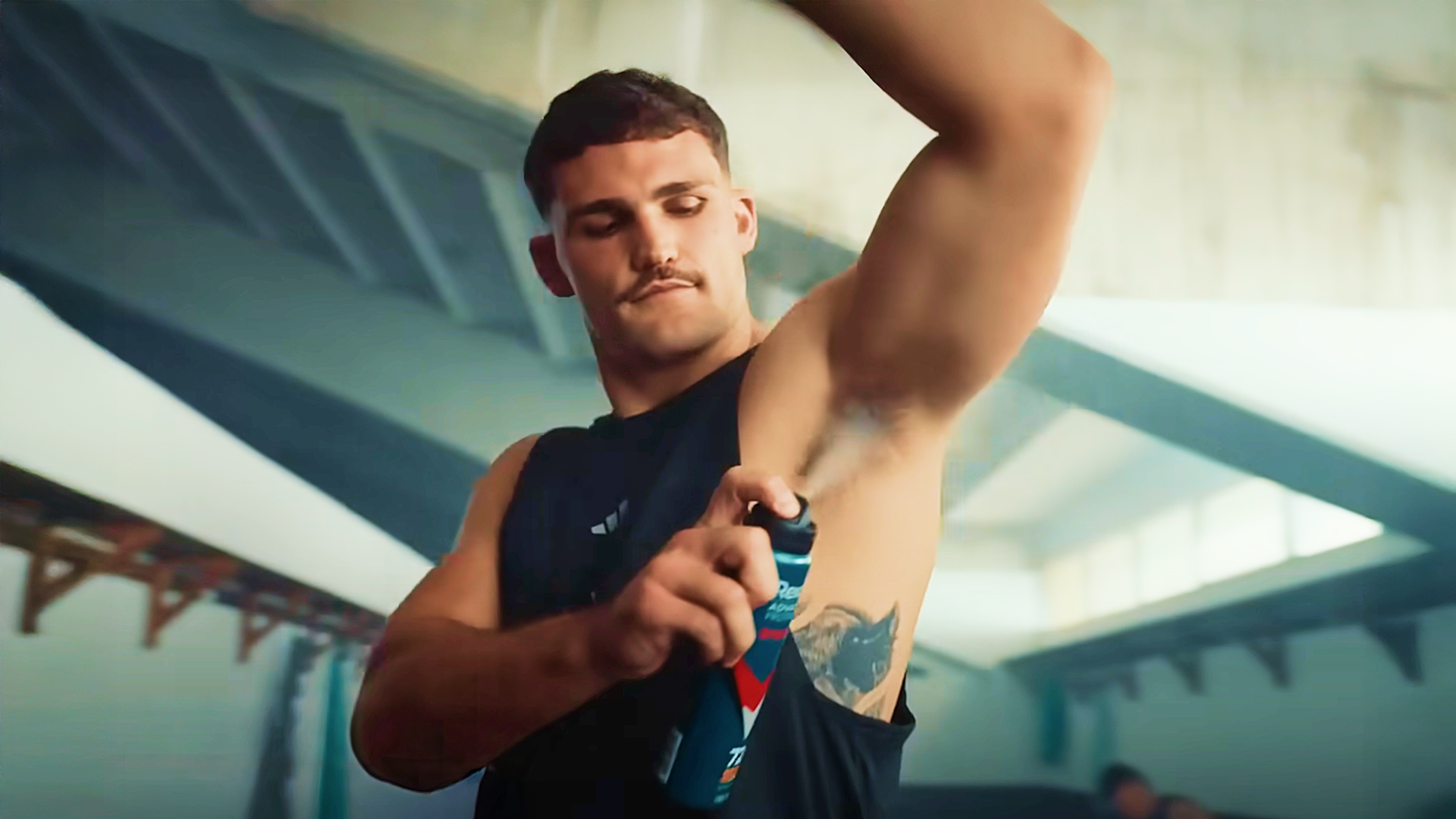 A man dressed for the gym confidently applies deodorant to his underarm.