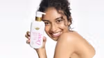 A person holding a Dove moisturising body lotion bottle with gold accents, shown against a bright, clean background.