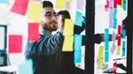 Young people learning from colourful stickers glued on glass wall during collaborative process in office