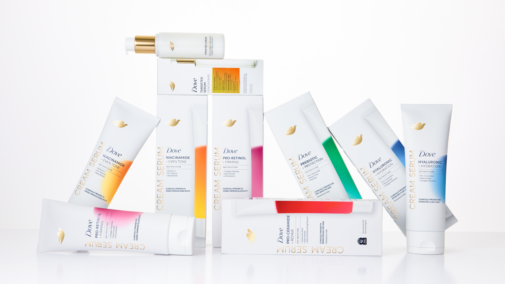 An arrangement of Dove cream serum from the Premium Body Care range. White tubes and bottles, each featuring colourful gradient labels, displayed upright and leaning against one another on a clean white background.