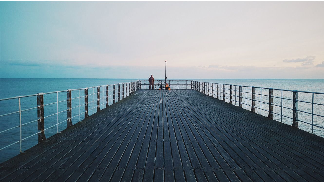 An image of a person on a pier looking out to the sea