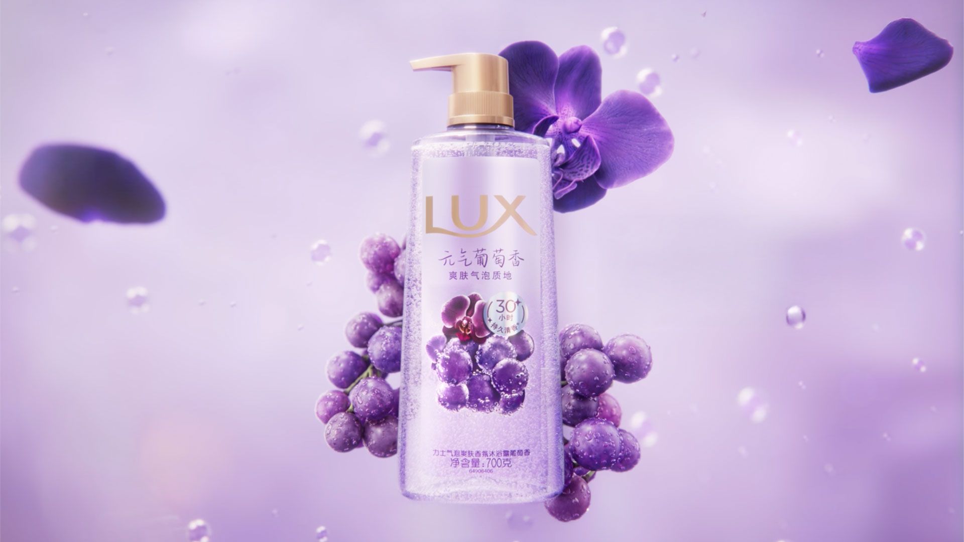 A transparent pump bottle of LUX body wash floats in a dreamy purple scene. The bottle contains shimmering purple liquid and is surrounded by fresh purple grapes, orchid petals, and soft-focus bubbles. The background is a gradient of lavender shades, and the overall atmosphere is light, fragrant, and floral.