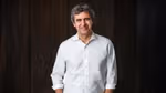 Fernando Fernandez in a white shirt standing against a dark wooden background