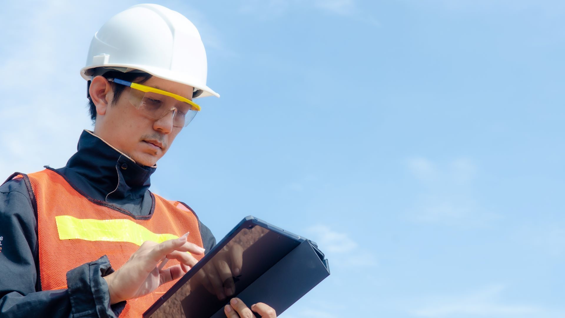 Man looking at clipboard outside in high visibility vest and safety goggles. 