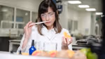 Person in a lab coat holding an orange slice with cosmetic ingredients