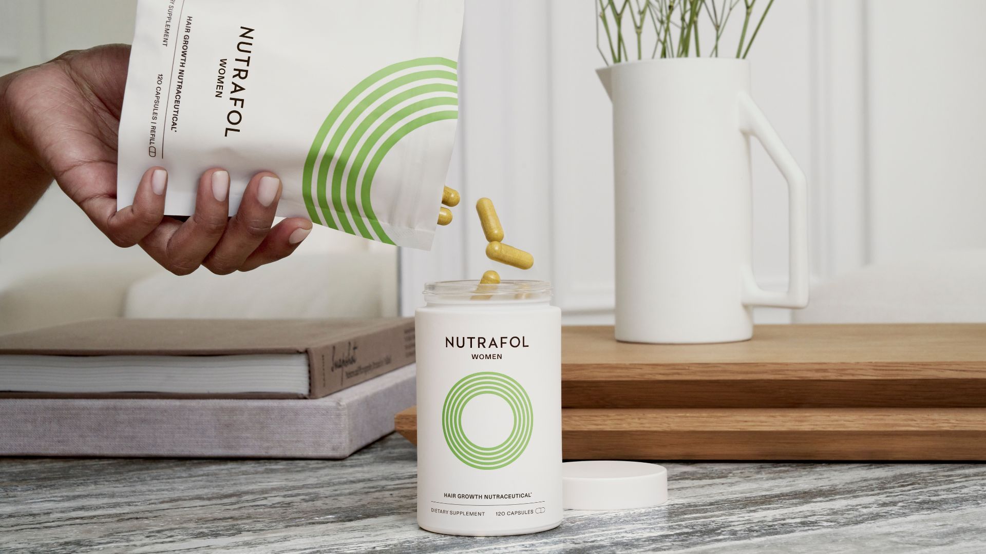 A woman’s hands, pouring yellow Nutrafol hair growth supplements from a refill bag into a white container.