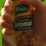 A hand grabbing a container of Knorr Universal Aromat to use as a condiment while cooking.