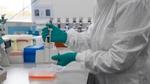A scientist at work in a Unilever R&D lab. Their face is not visible. They are wearing a white lab coat and green gloves, holding a device.