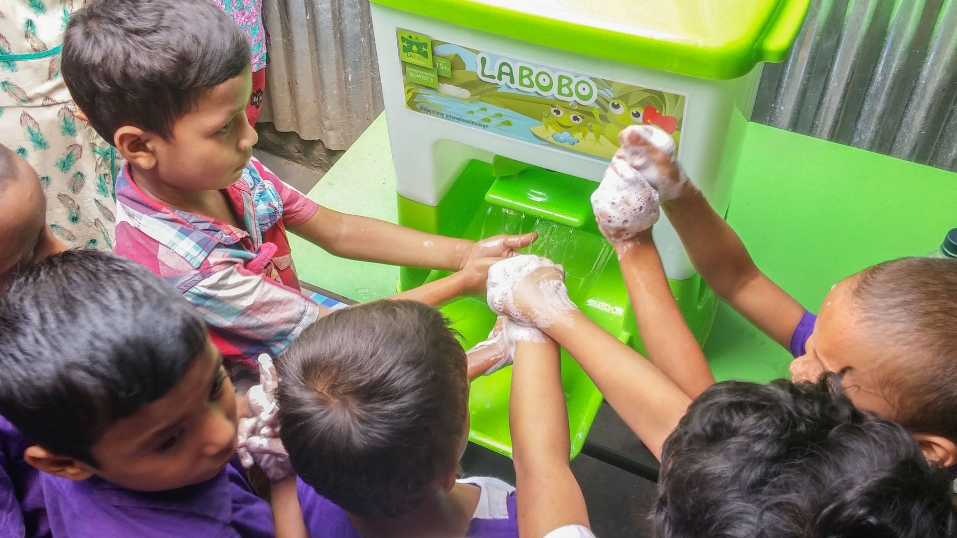 Group of small children washing their hands with soap using a HappyTap portable sink.