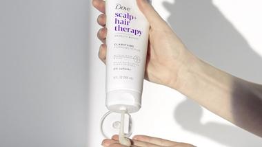 White product being squeezed out of a Dove scalp + hair therapy bottle.