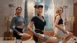 Three individuals performing a fitness or dance routine indoors, each holding a cylindrical object in one hand, with a large window and vintage decor in the background.