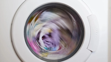 Zoomed in shot of a white washing machine with colourful clothes inside during a wash cycle.