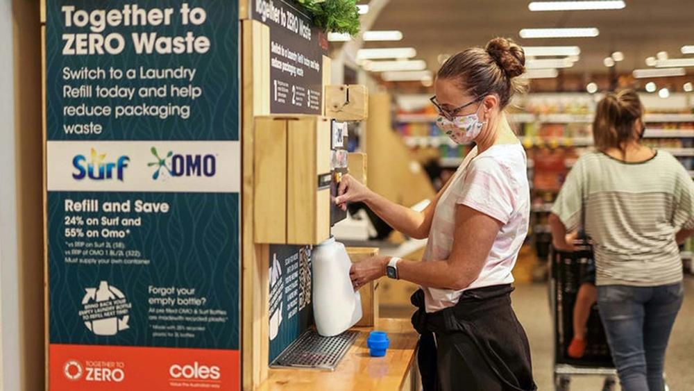 Woman filling a plastic bottle from an in-store refill machine that dispenses Surf and OMO products.