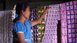 Woman store owner hanging up a sheet of sachets of Clear shampoo. Also visible are sachets of Rin, Bru, Sunsilk and Comfort.